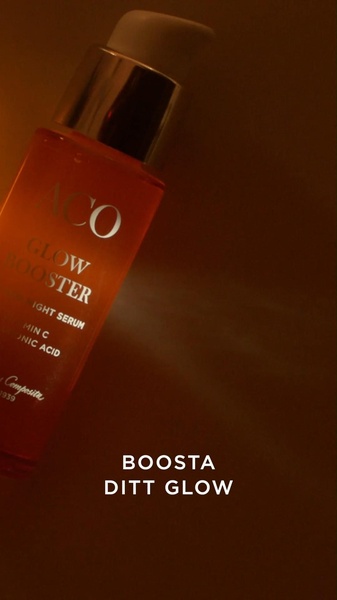 A high-contrast, low-light product shot of a Glow Booster night serum bottle set against a warm, amber-toned background.